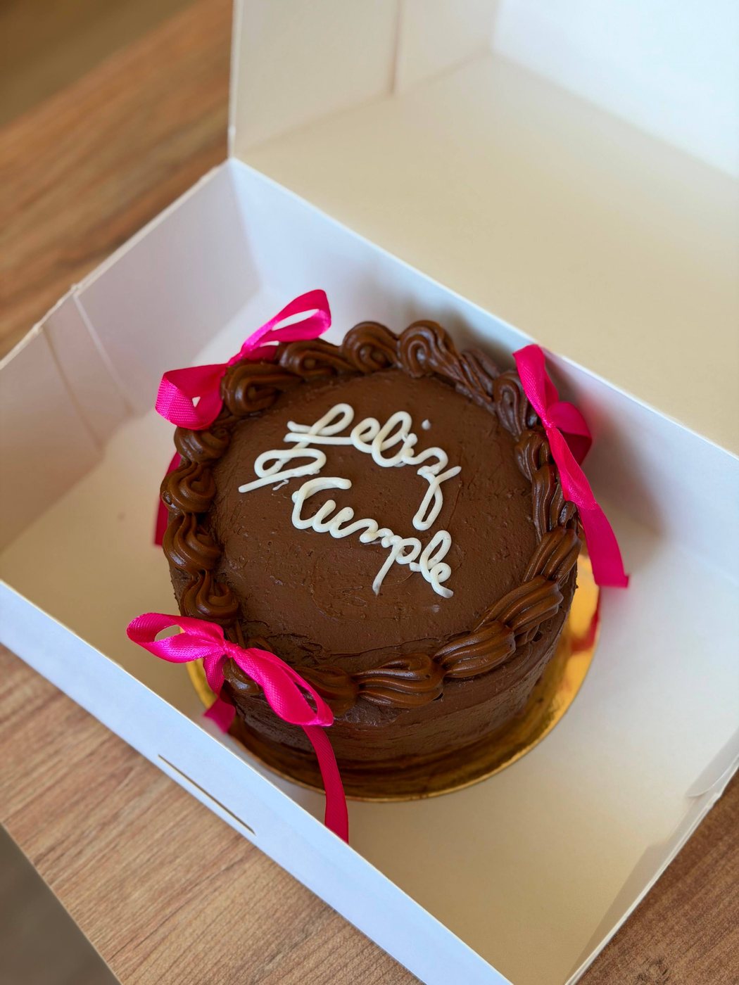 Pastel de chocolate con «Feliz cumple» escrito a mano y lazos